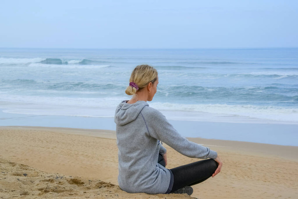 Békés, egészséges és fitt fiatal nő meditál a parton. Jóga a tengerparton. Nő meditál lótuszpózban. - Fotó, kép
