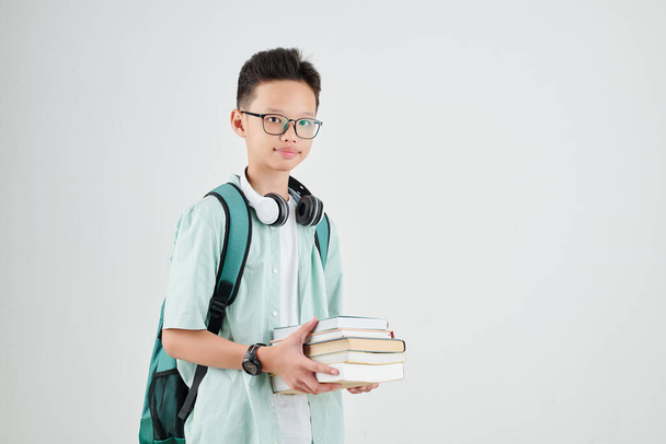 Studio portrait of smart schoolboy with backpack and stack of books looking at camera - Fotoğraf, Görsel
