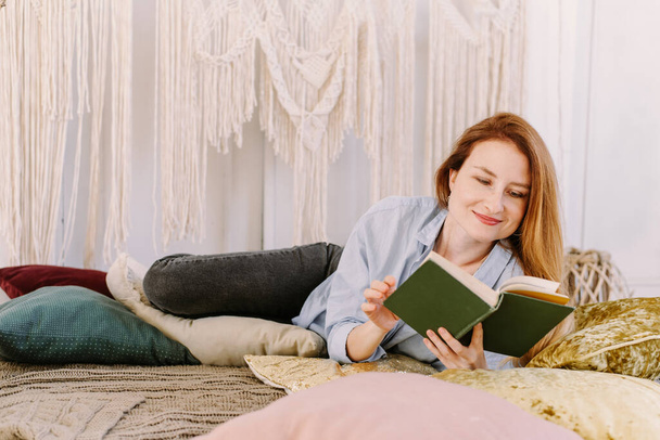 Jeune jolie femme lit un livre à la maison au lit. Concept de lecture de maison, intérieur lumineux. - Photo, image