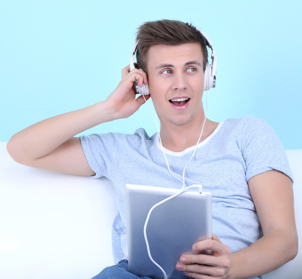 Guy sitting on sofa and listening to music on blue background - Zdjęcie, obraz