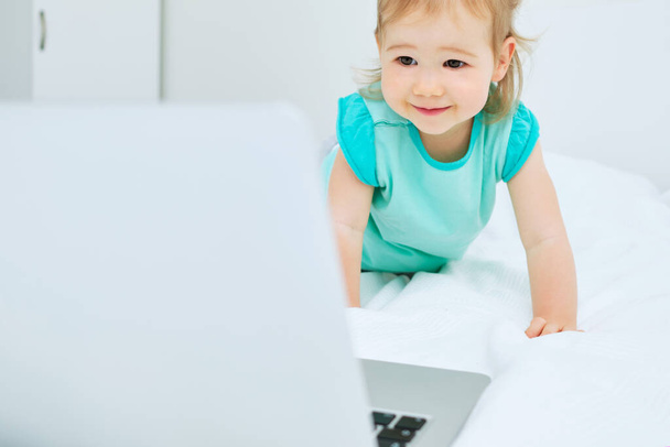 Happy smiling caucasian toddler girl at home with laptop on bed. - Photo, Image