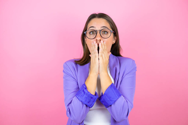 Young beautiful business woman over isolated pink background with her hands over her mouth and surprised - Photo, Image