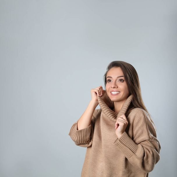 Young woman in stylish brown sweater on grey background, space for text - Valokuva, kuva