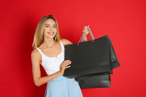 赤い背景にショッピングバッグを持つ幸せな若い女性。ブラック・フライデーセール - 写真・画像