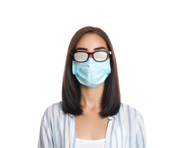 Молодая женщина в туманных очках, вызванных ношением одноразовой маски на белом фоне. Защитные меры во время пандемии коронавируса - Фото, изображение