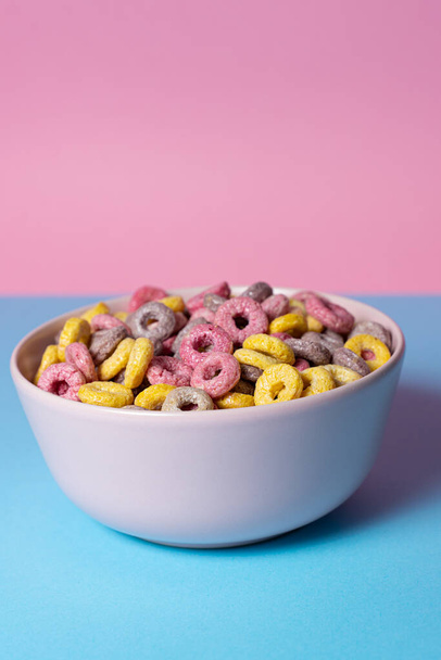 Geïsoleerde kom van gemengde granen en marshmallows op een blauwe en roze achtergrond - Foto, afbeelding
