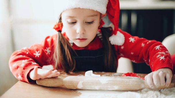 Lovely girl in christmas clothes preparing dough for holidays cookies at home - Photo, Image