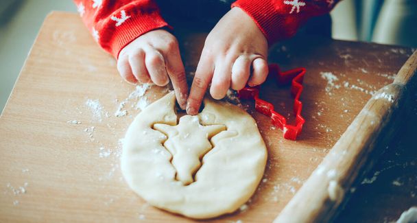 Χριστουγεννιάτικη προετοιμασία ενός μικρού παιδιού που φτιάχνει μπισκότα στο σπίτι φορώντας κόκκινο πουλόβερ - Φωτογραφία, εικόνα