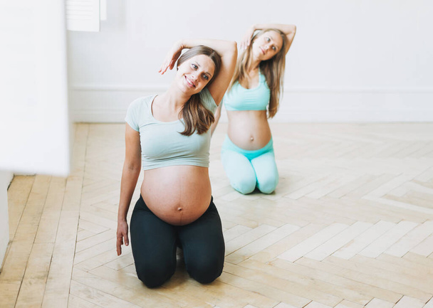Gruppe schwangere Frauen in Sportuniformen turnt im hellen Studio - Foto, Bild