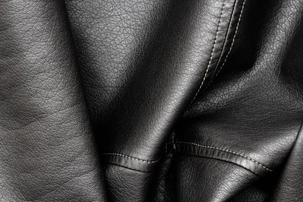 Close-up van zwarte stijlvolle en mode PU leren jas textuur met het getextureerde oppervlak en nette naainaden, geïsoleerd, achtergrond. Donker vintage motorjack van skai materiaal van bovenaf. - Foto, afbeelding