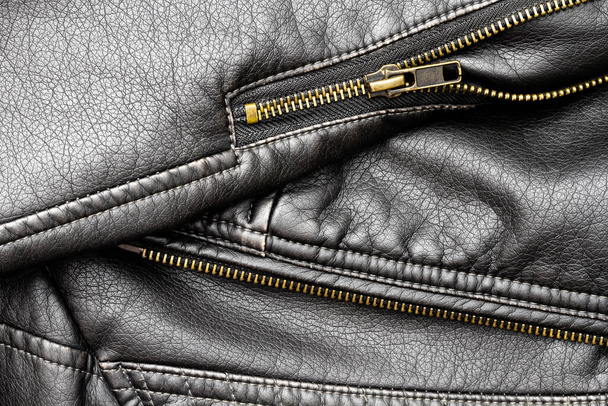Close up of black stylish and fashion PU leather biker jacket texture with the textured surface, neat sewing seams, and vintage copper-plated zipper with elements, isolated, from above, background. - Photo, Image
