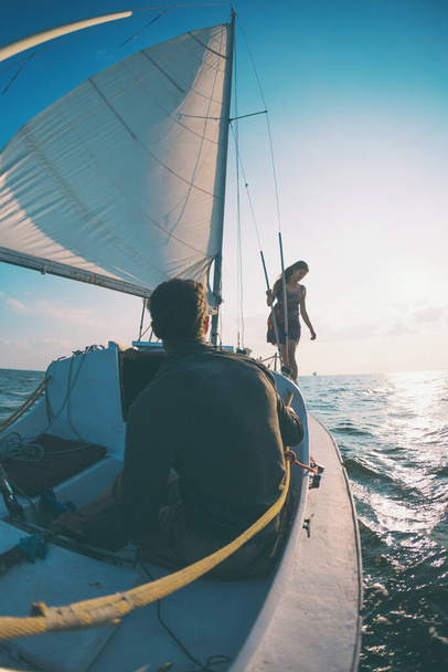 Romantikus szerelmesek a vitorlás hajón napnyugtakor a jachton, egy férfi és egy nő egy vitorlás jachton utaznak.. - Fotó, kép