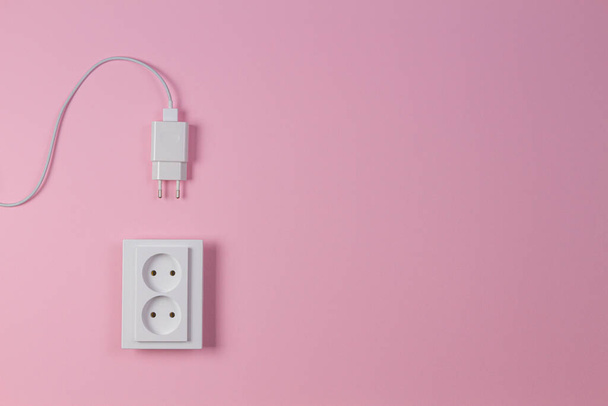 Fehér elektromos konnektor és tápcsatlakozó világos rózsaszín háttérrel. Felülnézet - Fotó, kép