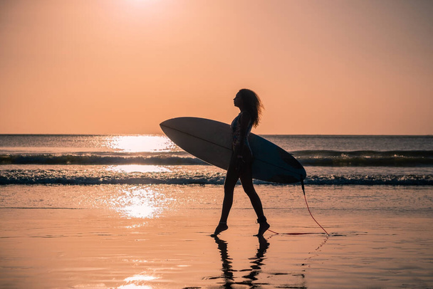 Portrait of woman surfer with beautiful body on the beach with surfboard at colorful sunset in Bali - Fotografie, Obrázek