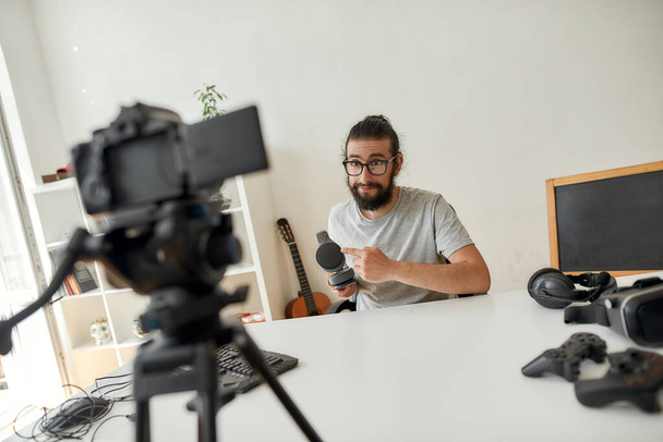 Male technology blogger holding, pointing at headphones while recording video blog or vlog about new gadgets at home studio - Foto, immagini