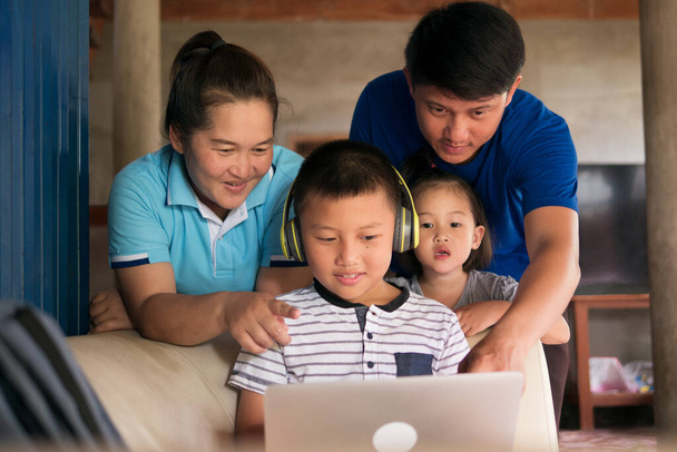 Homeschooling Kind Junge im Kopfhörer mit Laptop-Computer mit glücklichen asiatischen Familie Zusammensein in ländlichen Haus, Eltern helfen Kind bei den Hausaufgaben während COVID-19 Pandemie. - Foto, Bild