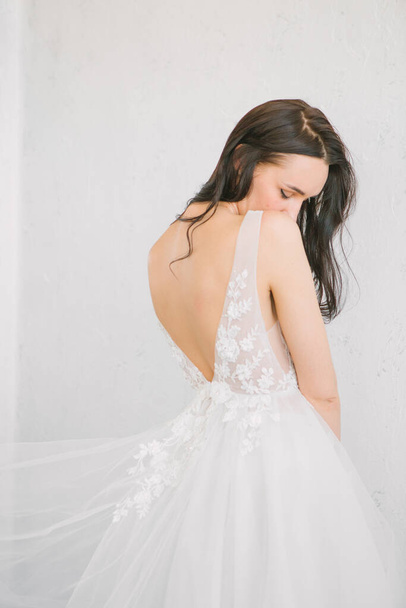 brunette bride with her back in a beautiful dress on a white background - Foto, Imagen