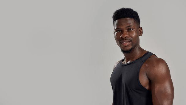Young muscular african american man looking at camera, while posing isolated over grey background. Sports, workout, bodybuilding concept - Zdjęcie, obraz
