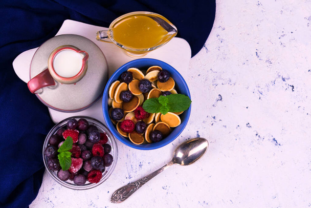 Mini crêpes aux baies congelées et miel et une cruche de lait sur la table. Pose plate. Espace de copie. - Photo, image