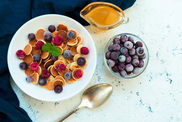 Завтрак из мини блинов с ягодами и медом, украшенный мятой на черном фоне.. - Фото, изображение