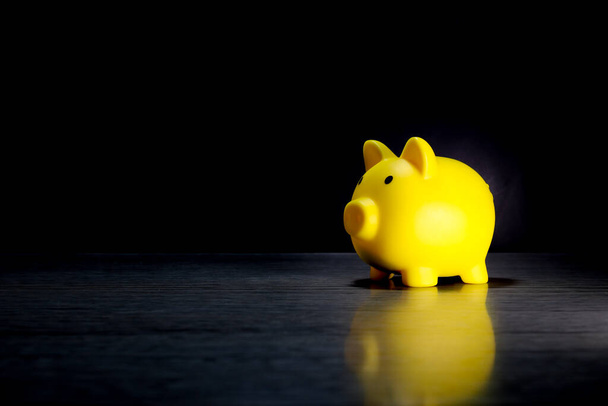 Gele varkens spaarpot geplaatst op bureau zwarte achtergrond (financiële planning concept) - Foto, afbeelding