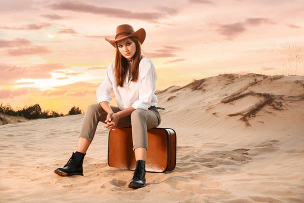 Beautiful fashionable young woman with suitcase in desert - Photo, image
