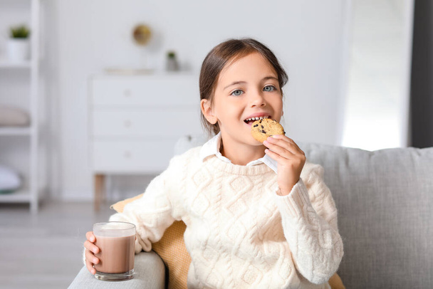 Niña bebiendo sabrosa leche de chocolate y comiendo galletas en casa - Foto, Imagen