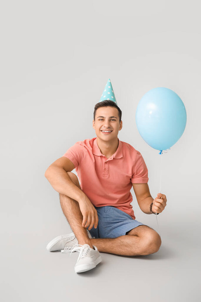 Nuori mies ilmapallo ja syntymäpäivä hattu harmaalla pohjalla - Valokuva, kuva