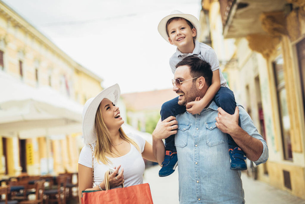 Ευτυχισμένη οικογένεια με μικρό παιδί και τσάντες ψώνια στην πόλη. - Φωτογραφία, εικόνα