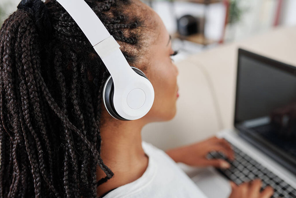 Pretty young woman with dreadlocks listening to good music in headphones when working on laptop at home - Fotoğraf, Görsel