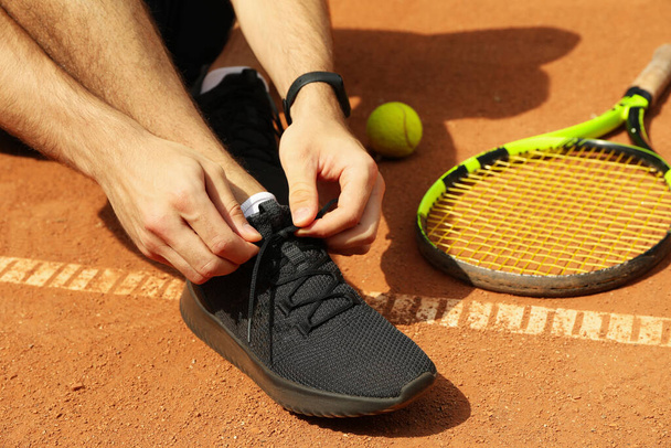 Man ties his shoelaces on clay court with racket and ball - Fotografie, Obrázek