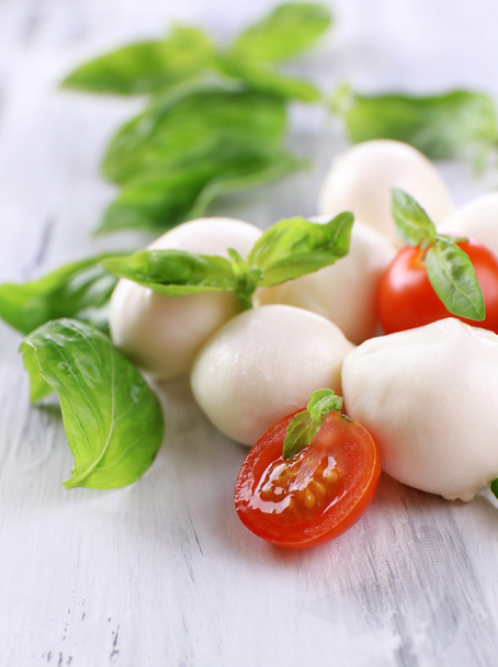 Tasty mozzarella cheese with basil and tomatoes, on wooden table - 写真・画像