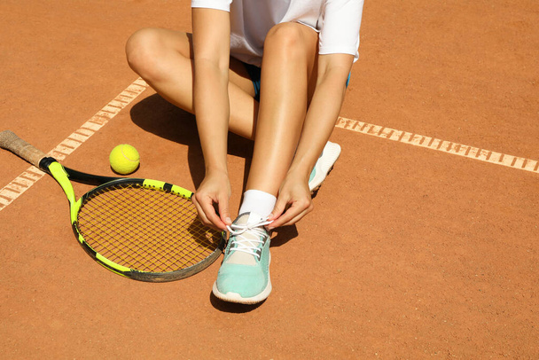 Woman ties shoelace on clay court with racket and and ball - Foto, afbeelding