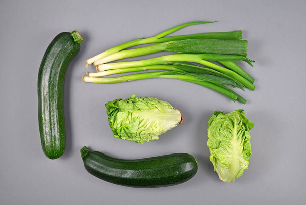 Változása zöld zöldségek, beleértve az újhagyma, cukkini és romain saláta szürke alapon, felső nézet lapos tojásrakás  - Fotó, kép