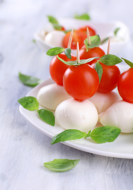 Tasty mozzarella cheese with basil and tomatoes on plate, on wooden table - 写真・画像
