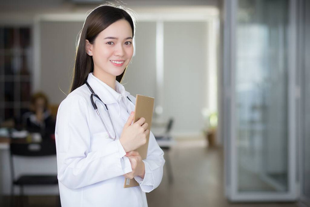 Ázsiai nő orvos mosolyog és magabiztosan áll, miközben ő tartja a dokumentum írótábla a kezében. - Fotó, kép