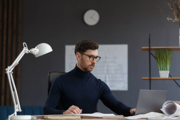 Architect working in office with blueprints.Engineer inspect architectural plan, sketching a construction project.Portrait of handsome bearded man sitting at workplace. Business construction concept - Foto, Imagem