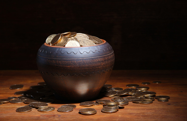 Golden coins in ceramic pot, on wooden table on dark background - Φωτογραφία, εικόνα