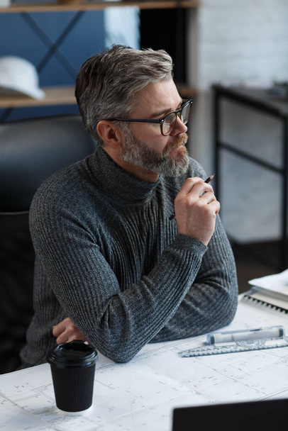 Interior designer working in office with blueprints.Engineer inspect architectural plan, sketching a construction project.Portrait of handsome bearded man at workplace. Business construction concept - Photo, image