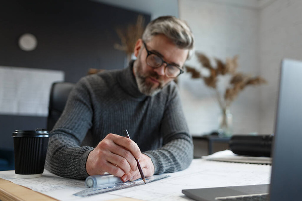 Interior designer working in office with blueprints.Engineer inspect architectural plan, sketching a construction project.Portrait of handsome bearded man at workplace. Business construction concept - Foto, afbeelding