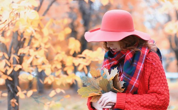 Young woman in a hat walks in park. Girl in autumn city park in leaf fall - Photo, Image