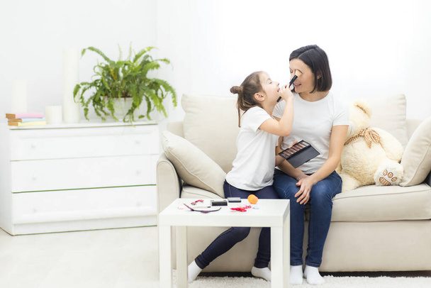 Photo of child girl doing make up for her mother on sofa. - 写真・画像