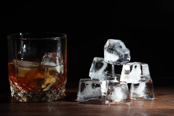 Ένα ποτήρι δυνατό αλκοολούχο ποτό με πάγο σε ξύλινο πάγκο μπαρ. Ουίσκι με παγάκια. Ποτήρι με παγωμένο ποτό. - Φωτογραφία, εικόνα