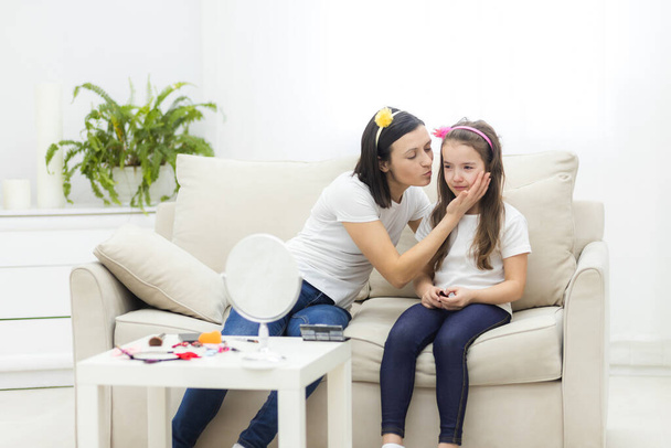 Full length photo of young mom sitting on sofa kissing small daughter. - Fotoğraf, Görsel