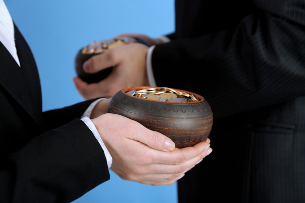 Two ceramic pots with golden coins in male and female hands, on color background - Foto, afbeelding