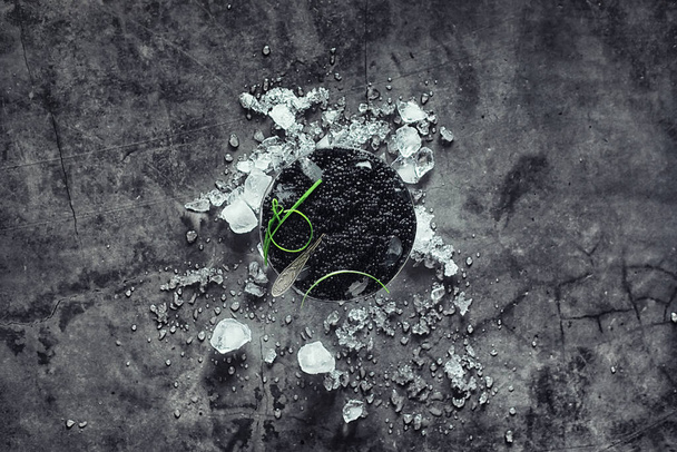 Fresh black fish roe. Beluga caviar served with ice with green. - Photo, Image