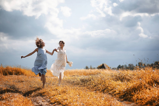 Δύο όμορφα κορίτσια σε φορέματα στον τομέα του φθινοπώρου διασκεδάστε - Φωτογραφία, εικόνα