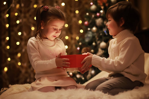 Famille le soir de Noël à la cheminée. Les enfants ouvrent des cadeaux de Noël. Enfants sous l'arbre de Noël avec des boîtes-cadeaux. Salon décoré avec cheminée traditionnelle. Cozy chaude maison de soirée d'hiver. - Photo, image