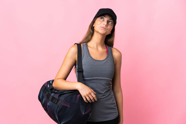 Young sport woman with sport bag isolated on pink background and looking up - Zdjęcie, obraz