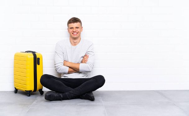 Young handsome man sitting on the floor with a suitcase laughing - Foto, Bild